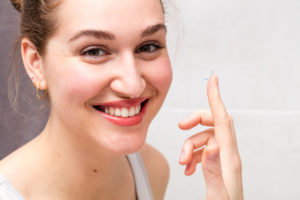 closeup portrait of a healthy young woman with a gorgeous smile holding a contact lens on her finger for farsighted, nearsighted or any optical eyesight solution from her bathroom