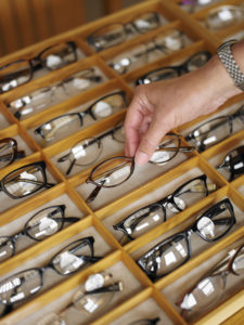 Man selecting a pair of eyeglasses from display case in shop, close-up of hand